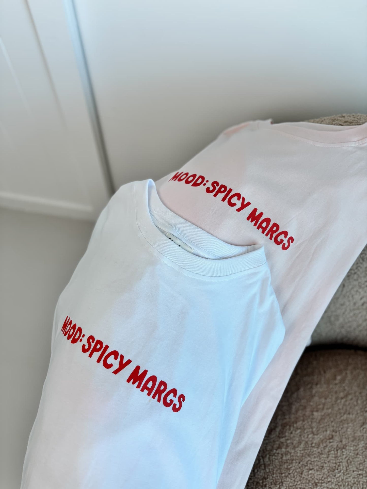 Front view of the 'MOOD: SPICY MARGS' oversized t-shirt in both blush pink and white, showcasing the 100% cotton fabric and relaxed fit.