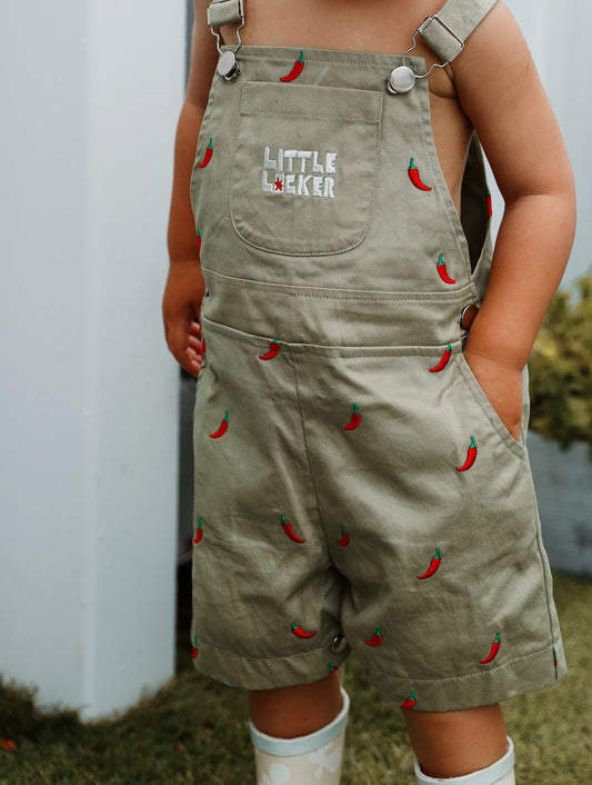 Toddler child wearing sage green overalls with red chili pepper pattern and 'Little Locker' logo.