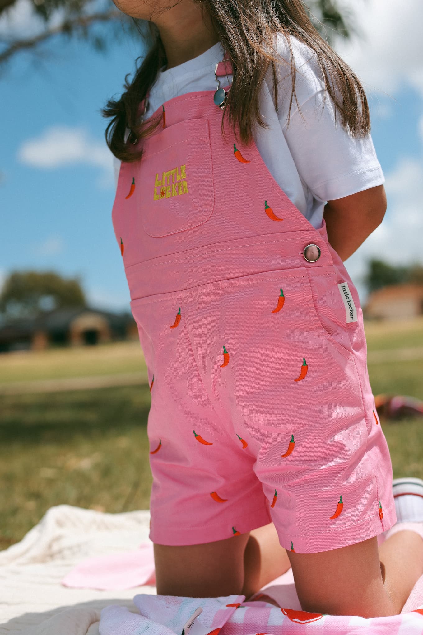 Girl wearing pink Little Locker cotton overalls with chilli pepper embroidery.