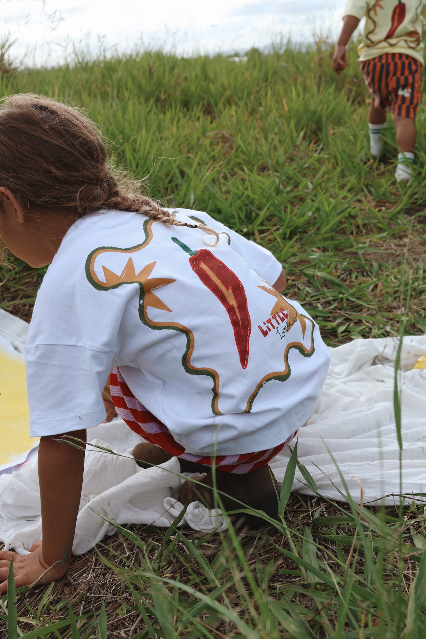Back view of a child wearing Little Locker's playful "MOOD: spicy" oversized white t-shirt with a vibrant red chilli graphic.