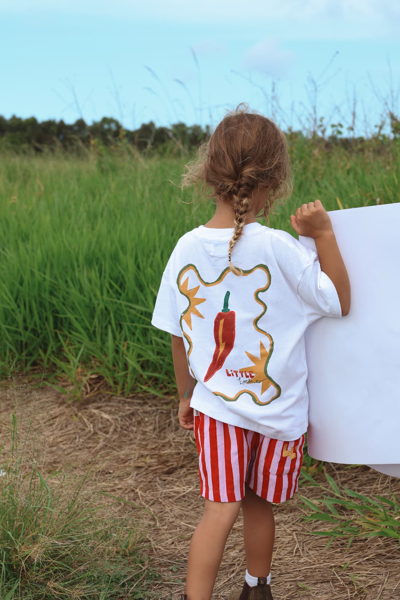 Child wearing an oversized white t-shirt with a red chilli design by Little Locker.
