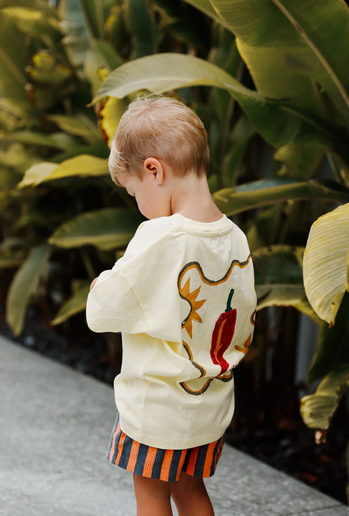 A stylish toddler wears Little Locker's "MOOD: spicy" yellow graphic t-shirt with striped corduroy shorts for a fun and modern look.
