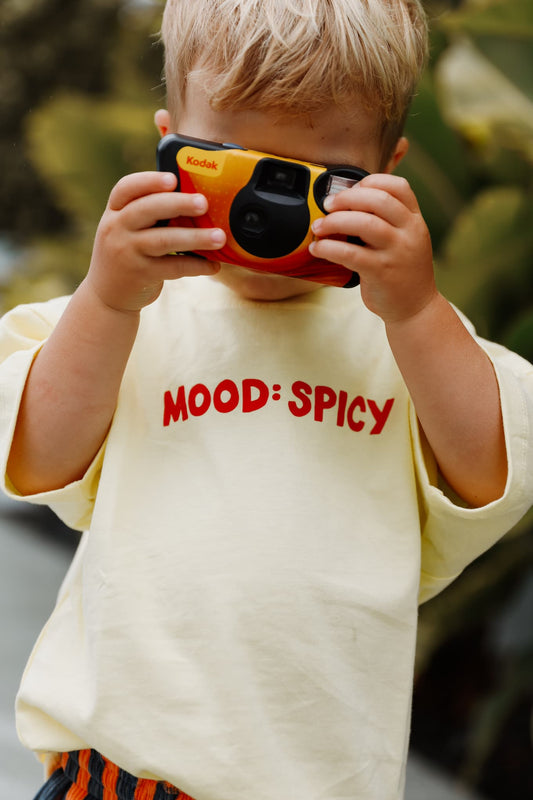 A stylish toddler pairs Little Locker's "MOOD: spicy" graphic t-shirt with striped corduroy shorts for a fun and modern look.