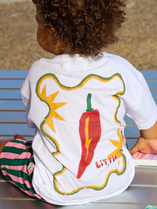 Child wearing Little Locker white t-shirt with colourful chilli design on back with striped shorts.